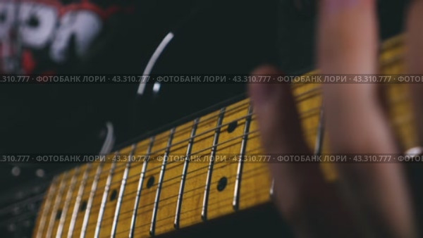 Close-up of a man's fingers with a green plectrum striking the top two strings of an electric guitar. The guitar has a black body. Slow motion of the vibration of the strings. Стоковое видео, видеограф Воловодов Владимир / Фотобанк Лори