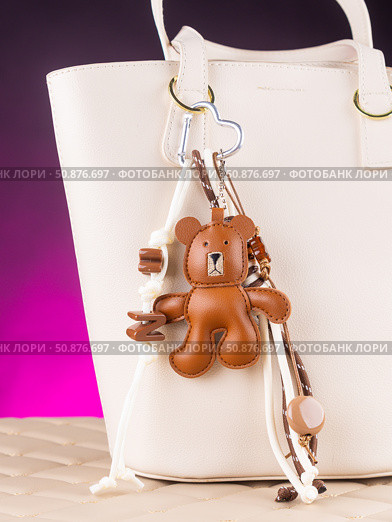 Close-up of a stylish leather bag accessory featuring a detailed leather bear charm no white bag. Стоковое фото, фотограф Виталий Сова / Фотобанк Лори