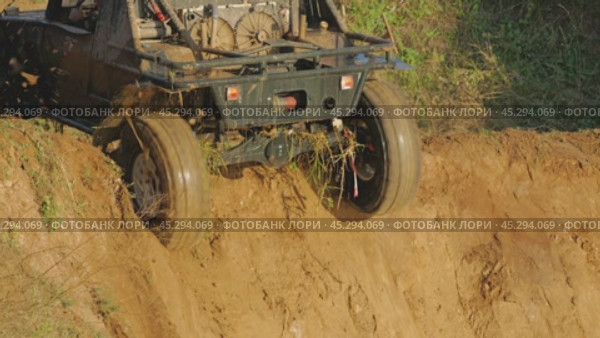 Close-up of an off-road buggy climbing a steep muddy hill. Water is pouring off the vehicle and mud is crumbling. The wheels are spinning fast, tugging and scattering dirt. Slow motion. Стоковое видео, видеограф Воловодов Владимир / Фотобанк Лори