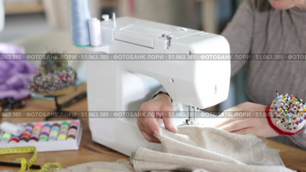 Close-up of professional female seamstress hands working at sewing machine, stitching checkered fabric with focus and precision at table in workshop. Стоковое видео, видеограф Яков Филимонов / Фотобанк Лори