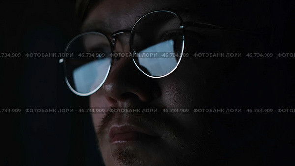 Close up of serious focused man scientist face in glasses looking at screen in the dark room. Стоковое фото, фотограф David Kashakhi / Фотобанк Лори