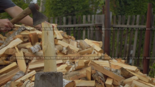 Close-up on axe embedded in wood while man applies force to chop logs. Logs stacked outdoors awaiting heating season. Стоковое видео, видеограф Strunov David / Фотобанк Лори