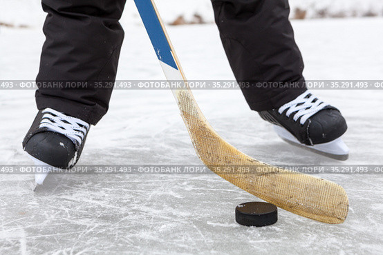 Close-up view at black puck and hockey skates on lake ice, teenage male legs, front view. Ноги хоккеиста и клюшка с шайбой. Стоковое фото, фотограф Кекяляйнен Андрей / Фотобанк Лори