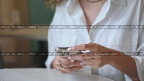 Closeup footage of young female using modern smartphone while sitting at table, cropped video of woman holding mobile phone, shopping online or browsing application. Стоковое видео, видеограф Ирина Михайличенко / Фотобанк Лори