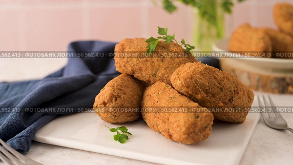 Cod dumplings, or "bolinhos de bacalhau" and parsley leaves on white ceramic dishes in a kitchen counter top. Стоковое фото, агентство Ingram Publishing / Фотобанк Лори