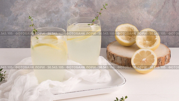 Cold lemonade or alcoholic cocktail with lemon, rosemary and ice in glass glasses on a light background. Стоковое фото, агентство Ingram Publishing / Фотобанк Лори