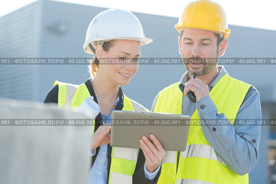 colleagues outdoors wearing reflective vests looking at tablet. Стоковое фото, агентство Ingram Publishing / Фотобанк Лори