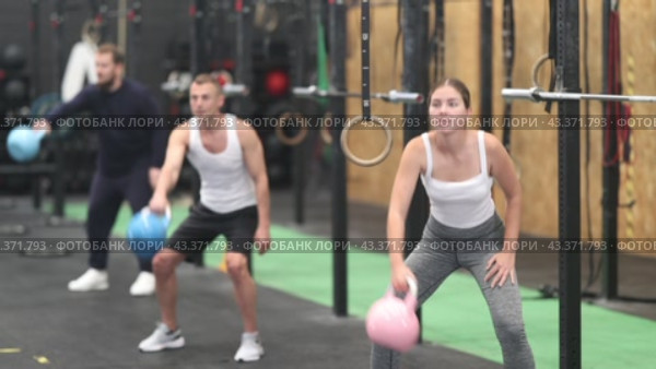Concentrated athletic young woman taking part in intense group training in modern gym, performing exercises with kettlebells. Fitness and bodybuilding concept. Стоковое видео, видеограф Яков Филимонов / Фотобанк Лори