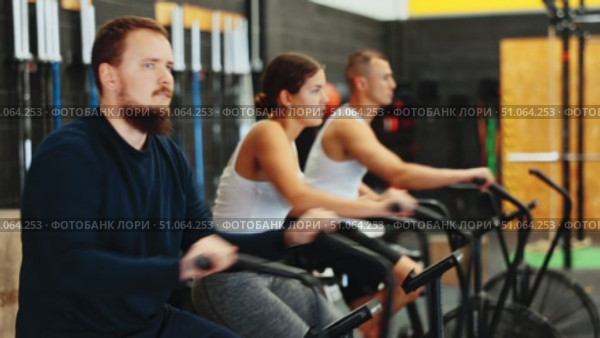 Concentrated sporty young bearded man intensely working out on stationary air bicycle in fitness gym. Healthy active lifestyle concept Focused motivated bearded guy leading healthy active lifestyle doing cardio workout on air resistance bike in gym. Стоковое видео, видеограф Яков Филимонов / Фотобанк Лори