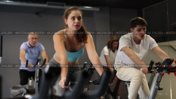 Concentrated young fit girl working out on stationary bicycle in gym. Healthy active lifestyle concept. Стоковое видео, видеограф Яков Филимонов / Фотобанк Лори