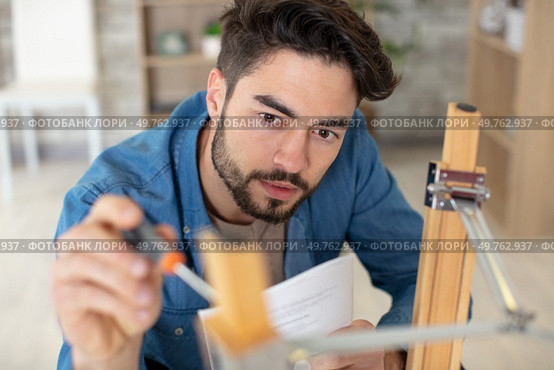 concentrated young man reading the instructions to assemble furniture. Стоковое фото, агентство Ingram Publishing / Фотобанк Лори