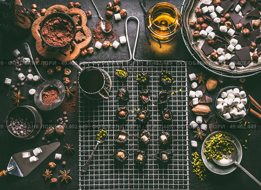 Confectionery or patisserie concept. Preparation of pralines with prunes soaked in rum and stuffed with nuts, marshmallow and pistachio on dark table background with chocolate and ingredients. Стоковое фото, агентство Ingram Publishing / Фотобанк Лори