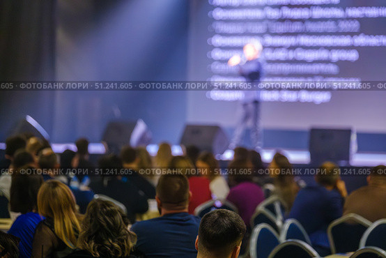 Conference speaker addressing audience on stage with large screen in background. Стоковое фото, фотограф Антон Гвоздиков / Фотобанк Лори