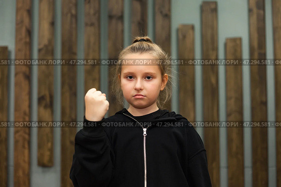 Confident Girl Demonstrating Strength With a Raised Fist in a Creative Indoor Setting. Стоковое фото, фотограф Aleksandr Golubev / Фотобанк Лори