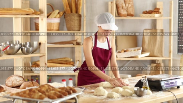 Confident teenage female learner shaping dough into rolls on the countertop in bakery. Стоковое видео, видеограф Яков Филимонов / Фотобанк Лори