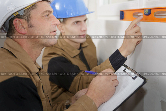 constructor showing assistant measuring the wall indoors. Стоковое фото, агентство Ingram Publishing / Фотобанк Лори