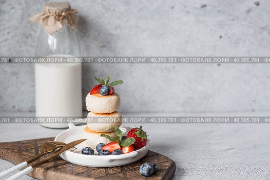 Cottage cheese pancakes, Russian cheesecakes with fresh blueberries, strawberries and mint on a stylish wooden board on a gray concrete table. Natural products. Healthy and delicious breakfast. Стоковое фото, фотограф Photojuli / Фотобанк Лори