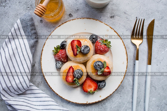Cottage cheese pancakes, Russian cheesecakes with fresh blueberries, strawberries, honey and mint leaves on a stylish wooden board on a gray concrete table. Natural products. Healthy and delicious breakfast. Стоковое фото, фотограф Photojuli / Фотобанк Лори