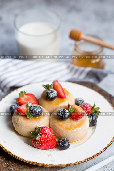 Cottage cheese pancakes, Russian cheesecakes with fresh blueberries, strawberries, honey and mint leaves on a stylish wooden board on a gray concrete table. Natural products. Healthy and delicious breakfast. Стоковое фото, фотограф Photojuli / Фотобанк Лори