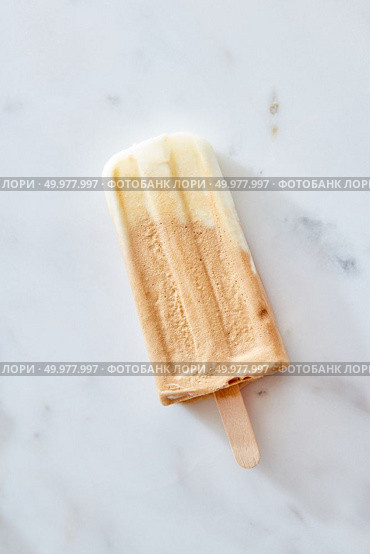 Creme brulee coffee ice cream on a wooden stick over marble background, top view. Healthy summer dessert. Frozen coffee gelato ice cream on a wooden stick over marble background, top view. Summer delicious desserts. Стоковое фото, агентство Ingram Publishing / Фотобанк Лори