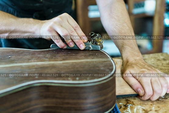 Crop craftsman using plane to shave traditional Spanish flamenco guitar on workbench in workshop. Unrecognizable male luthier crafting Spanish flamenco guitar. Стоковое фото, агентство Ingram Publishing / Фотобанк Лори