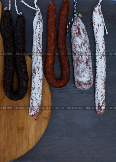 Cured meat and sausages hanging on dark wooden background. Cured meat and sausages. Стоковое фото, агентство Ingram Publishing / Фотобанк Лори