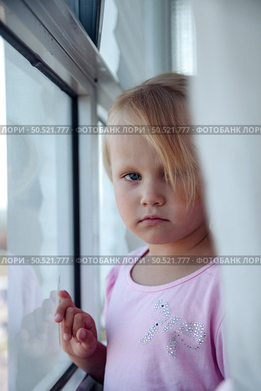 Curious Girl Gazes out the Window, Lost in Thought and Wonder at the World Beyond. Стоковое фото, фотограф Aleksandr Golubev / Фотобанк Лори