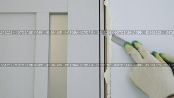 Cut off excess hardened polyurethane foam with a knife after foaming the cracks in the door frame. Construction and repair. Installation and fastening of a wooden frame. Стоковое видео, видеограф Дмитрий Кобзев / Фотобанк Лори