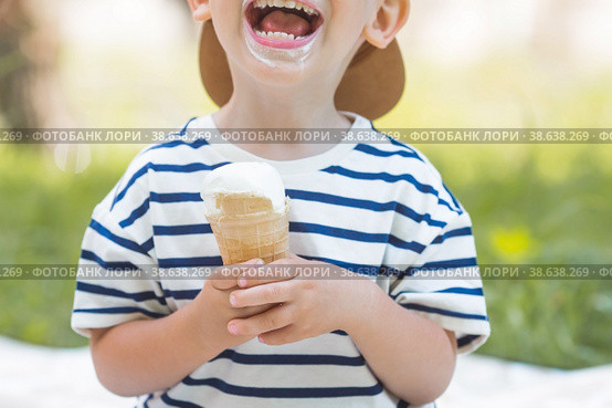 Cute, happy little boy with a beautiful smile and dirty face eating ice cream outdoors on a hot summer day. A child enjoys a sweet dessert during the summer holidays. Стоковое фото, фотограф Photojuli / Фотобанк Лори