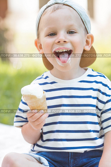 Cute, happy little boy with a beautiful smile and dirty face eating ice cream outdoors on a hot summer day. A child enjoys a sweet dessert during the summer holidays. Стоковое фото, фотограф Photojuli / Фотобанк Лори