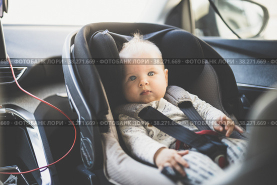 Cute little baby boy strapped into infant car seat in passenger compartment during car drive. Стоковое фото, фотограф Matej Kastelic / Фотобанк Лори