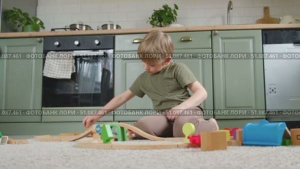 Cute little blonde child boy sitting on the floor playing with wooden toy train. Toddler kid plays railway. Made of natural materials. Birthday gift. Preschool employment. Brain, coordination exercise. Стоковое видео, видеограф Марина Демидюк / Фотобанк Лори