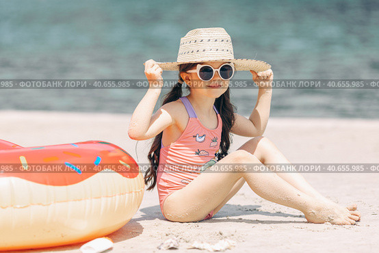 Cute little girl sitting on the sand on a beach in a swimsuit and straw hat. Стоковое фото, фотограф Ирина Михайличенко / Фотобанк Лори