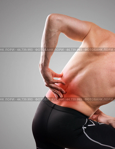 Damage to the lumbar spine. Man holds his back in pain, on a gray background. The concept of human injury, lumbago. Стоковое фото, фотограф Дмитрий Кобзев / Фотобанк Лори