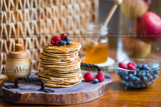 Delicious pancakes with honey, blueberries and raspberries. Next to it is a wooden barrel with an inscription in Russian: "honey". The concept of the Maslenitsa holiday. Стоковое фото, фотограф Photojuli / Фотобанк Лори