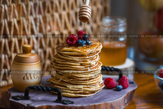 Delicious pancakes with honey, blueberries and raspberries. Next to it is a wooden barrel with an inscription in Russian: "honey". The concept of the Maslenitsa holiday. Стоковое фото, фотограф Photojuli / Фотобанк Лори