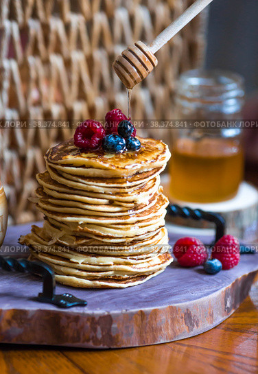 Delicious pancakes with honey, blueberries and raspberries. Next to it is a wooden barrel with an inscription in Russian: "honey". The concept of the Maslenitsa holiday. Стоковое фото, фотограф Photojuli / Фотобанк Лори