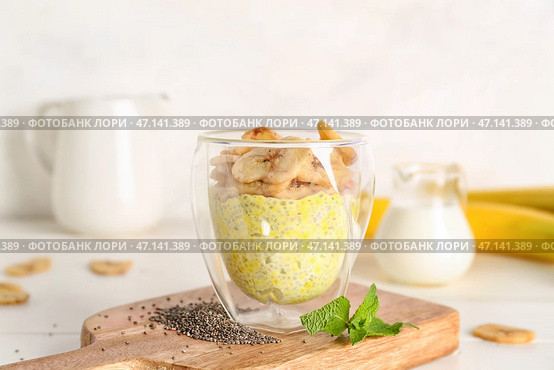 Деревянная доска со стаканом вкусного пудинга из семян чиа и бананом на светлом столе. Стоковое фото, фотограф Pixel_shot / Фотобанк Лори