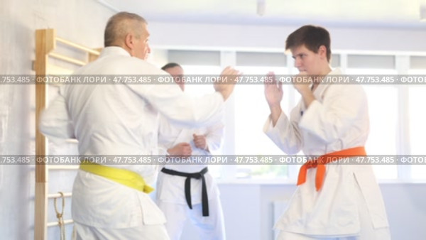 Determined motivated senior man wearing kimono working on hand strikes and martial arts skills in sparring with young opponent during group training. Стоковое видео, видеограф Яков Филимонов / Фотобанк Лори