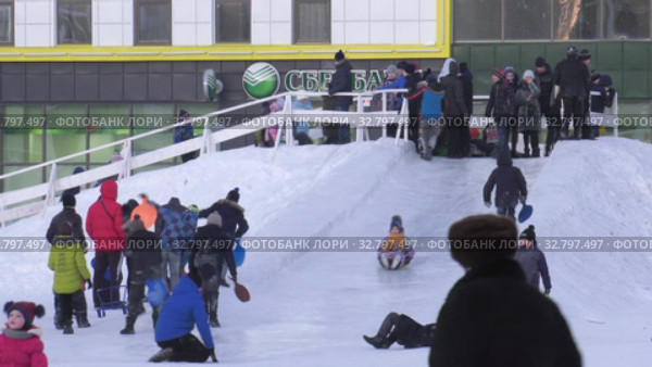 Дети катаются с ледяной горки на городской площади. Children ride on an ice slide in the town square. (2019 год). Редакционное видео, видеограф Евгений Романов / Фотобанк Лори