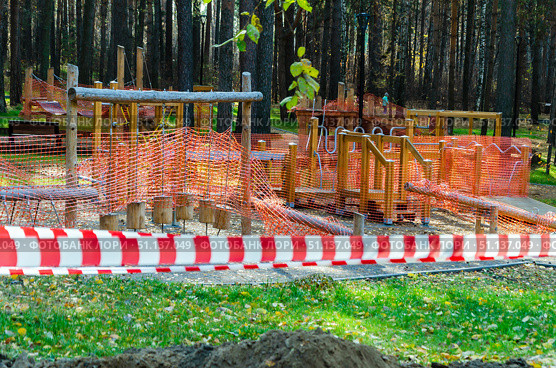Детская площадка в парке огорожена оранжевой защитной сеткой и красно-белой оградительной лентой. Ремонт на детской игровой площадке в городском парке. Стоковое фото, фотограф Нина Чалых / Фотобанк Лори