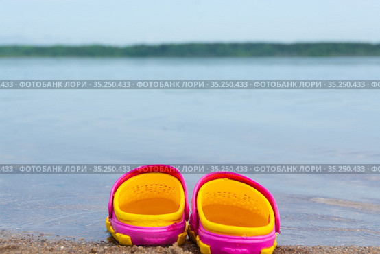 Детские розовые сабо стоят на песчаном пляже около воды. Children's pink clogs stand on a sandy beach near the water. Стоковое фото, фотограф Мария / Фотобанк Лори