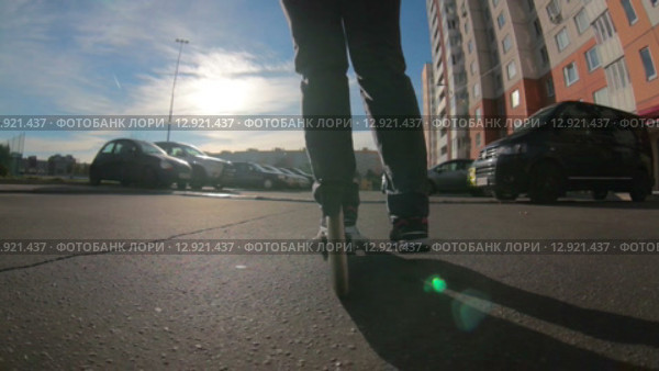 Девушка едет на самокате по асфальтовой дороге среди припаркованных автомобилей во дворе, вид сзади и снизу (2015 год). Редакционное видео, видеограф Кекяляйнен Андрей / Фотобанк Лори