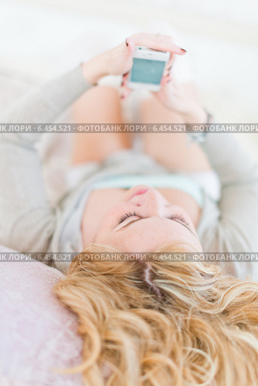Девушка переписывается с помощью смартфона, лежа на кровати. Стоковое фото, фотограф Валерия Лузина / Фотобанк Лори