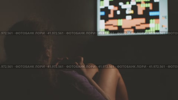 Девушка в темной комнате играет в приставку, сидя на стуле-мешке. Концепция домашних развлечений. Стоковое видео, видеограф Воловодов Владимир / Фотобанк Лори