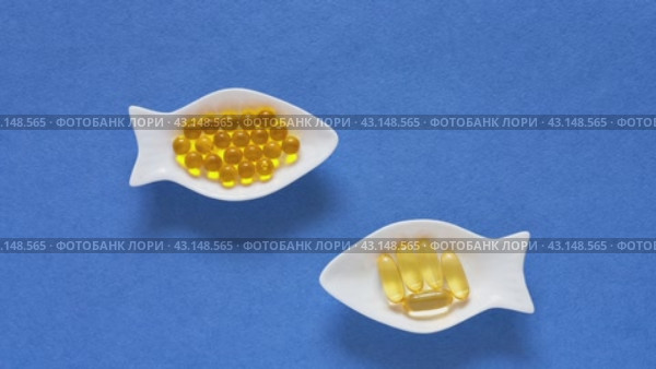 Dietary supplements or nutrition additions with fish oil, vitamin E and omega acids. Concept of preventing heart disease using fish oil. Flat lay of gelatin capsules on fish-shaped plates on blue background. Стоковое видео, видеограф Виктория Катьянова / Фотобанк Лори