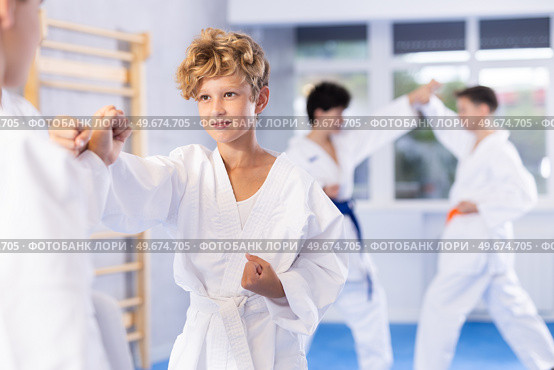Diligent preteen attendee of karate classes fighting with his opponent in sports hall. Стоковое фото, фотограф Яков Филимонов / Фотобанк Лори