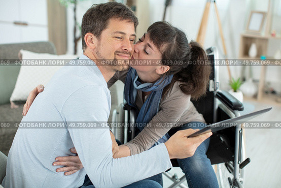 disabled woman kissing her husband holding a tablet. Стоковое фото, агентство Ingram Publishing / Фотобанк Лори