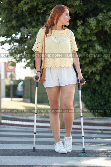 disabled young woman walking on crutches in street. Стоковое фото, агентство Ingram Publishing / Фотобанк Лори