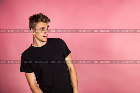 Dissatisfied young man looking unpleasantly away, expresses aversion, smirking at pink background. Guy in black t-shirt scared, negative face expressions concept. Advertising. Copy text space. Стоковое фото, фотограф Aleksandr Golubev / Фотобанк Лори